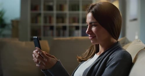 Woman Smiling at Phone While Relaxing on Sofa