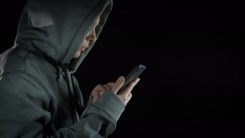 Person in Hoodie Using Phone Against Black Background