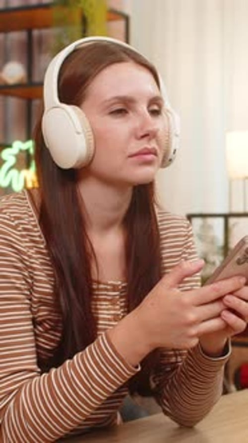 Young Woman Listening with Headphones Holding Phone Indoors
