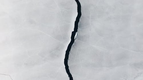 Drone View of a Crack with Water Splitting an Icy Frozen Surface Into Two Parts