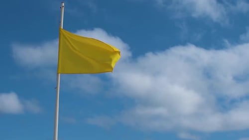 Yellow Warning Flag Waving Against Blue Sky