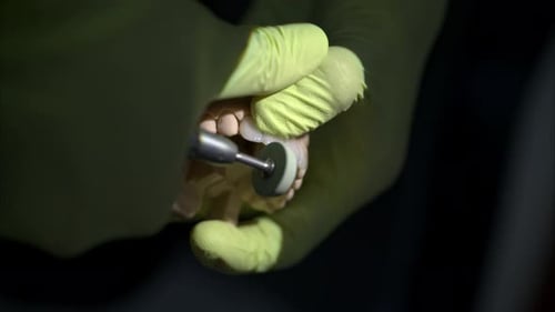 Slow motion close-up of a dentist pair of hands wearing green gloves filing a set of dental veneers