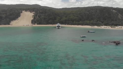 Aerial drone shot above a clear turquoise ocean and towards tourists, boats and a ferry, on a