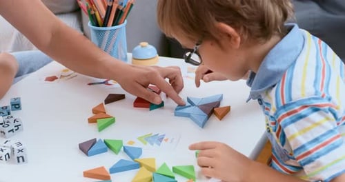 Child and Adult Hands Arranging Colorful Wooden Shapes on Table