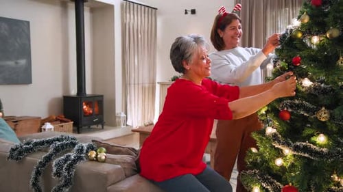 Senior women decorating Christmas tree at home, enjoying festive holiday spirit