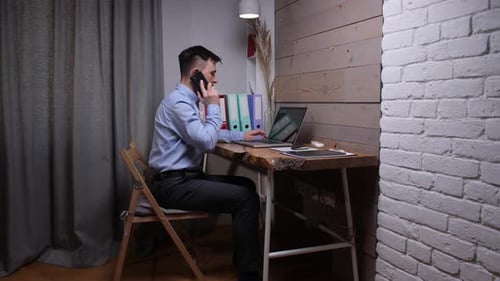 Man Working at Desk Using Laptop and Phone