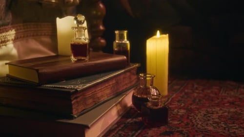 Mit dunkler Flüssigkeit gefüllte Flaschen und Bücher auf einem Vintage-Teppich neben glühender Kerze