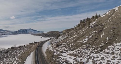 Winding Winter Road Alongside Frozen Lake Below Snow Dusted Mountains