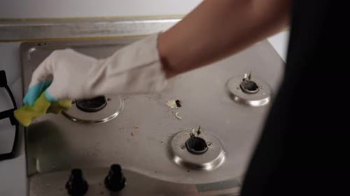 Gloved Hand Cleans Dirty Silver Stove Top