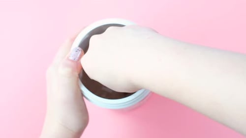 Chocolate protein powder in scoop and plastic jar on pink background, top view.