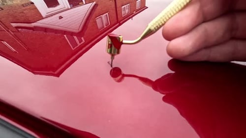 Touching in a scratch on a red car with fine touch up pen applicator - close up