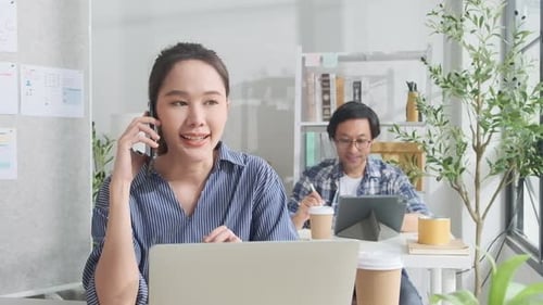 Two young Asian startup partners are working in a casual small business office.