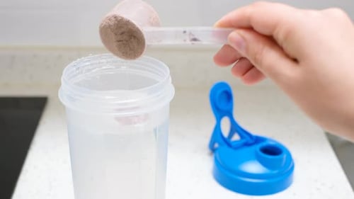 Female hand making chocolate protein shake side view.