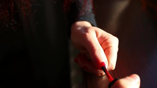 girl puts red nail polish on the nails of the hand