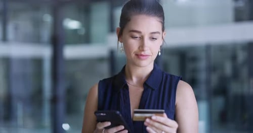 4k video footage of a young businesswoman using a cellphone and credit card in an office