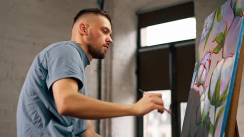Young Artist in a Blue Tshirt in an Art Studio Working on Painting While Sitting