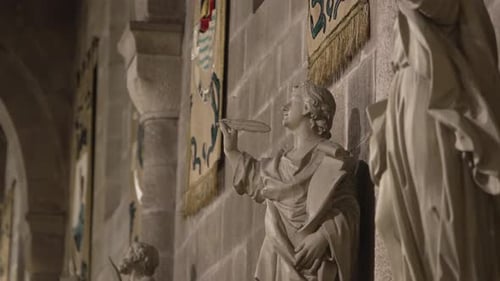 Close up of a stone statue holding a quill, with banners in the background inside Sé de Braga
