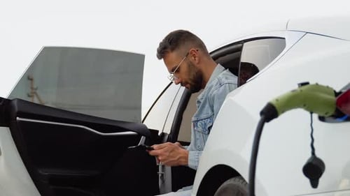 Man in Electric Car Charging Talks on Phone