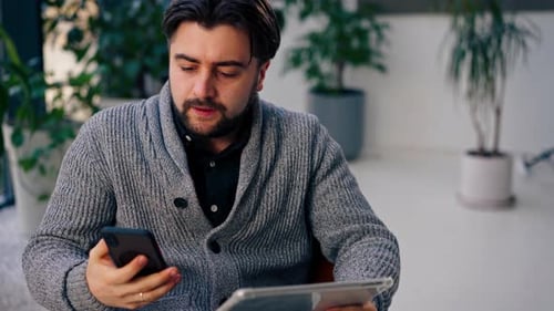 Close Up In a White Hall a Young Guy Office Worker on a Brown Chair with Tablet Talking on the Phone