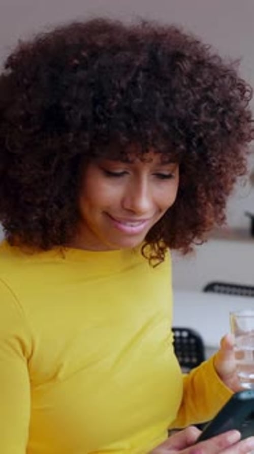 Young Woman Drinking Water While Using Mobile Phone at Modern Loft Apartment