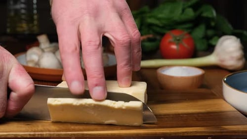 The Cook Cuts Hard Cheese with a Kitchen Knife and Puts a Piece of Cheese on a Cutting Board The