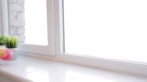 Hand Dusting Windowsill with Colorful Duster in Bright Room