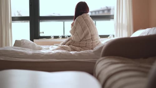 Woman Wrapped in Blanket Sitting on Bed