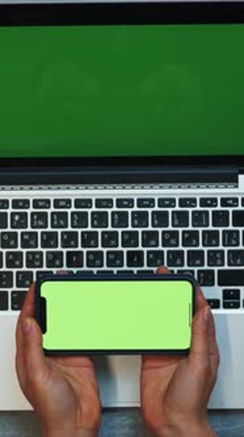 Woman works using laptop and smartphone with green screen. Vertical video