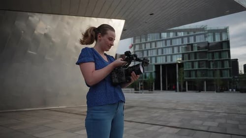 Woman Adjusting Professional Video Camera in Urban Setting
