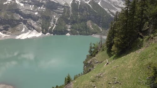 Mountain reflecting in the water of the Oeschinensee lake while flying past a steep overgrown hill o