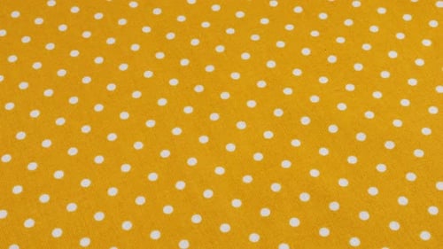 Top view of the amber yellow with white polka dots cotton fabric rotated on the display case.