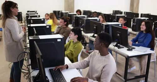 Ein reifer Lehrer arbeitet mit gemischtrassigen Studenten im Computerraum der Universität zusammen