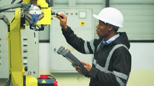 African American technician man hold controller pad of robotic arm machine and check and maintenance