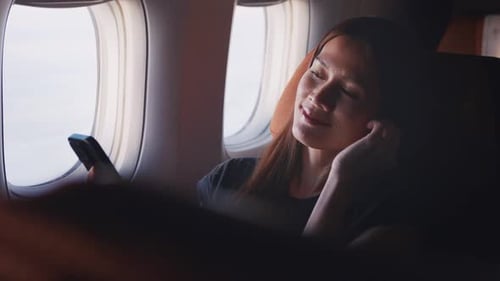 Asian woman using headphone listen to music while sitting in airplane.