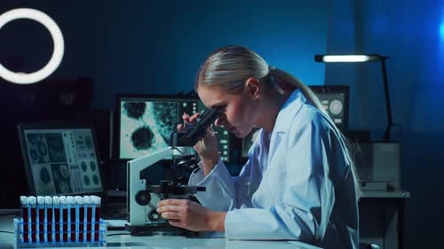 Scientist Analyzes Samples Under Microscope in Blue Lab