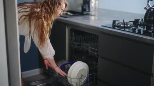 Woman Unloading Dishes From Dishwasher in Modern Kitchen