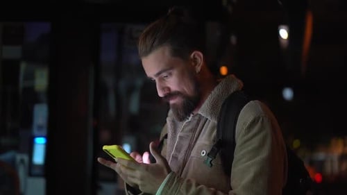 Caucasian Man Tourist Arriving to a City at Night By Bus Using Phone to Look for Hostels Direction
