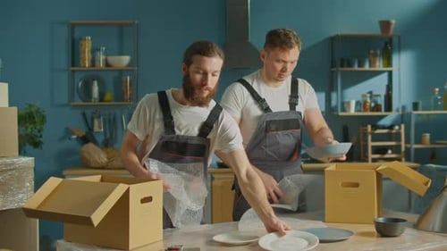 Workers of Moving Company With Uniforms Carefully Unpacking Dishes at Boxes