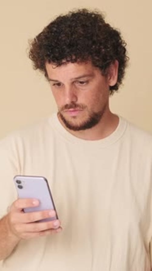 Surprised man with mobile phone in his hands in studio on beige background