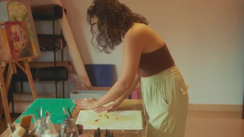 Female artist applying paint onto paper using tissue or paper for textured effect.