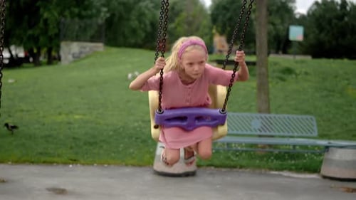 Pretty Little Girl Plays Swings in Urban Park on Waterfront Happy Child Enjoys Attraction on Ground
