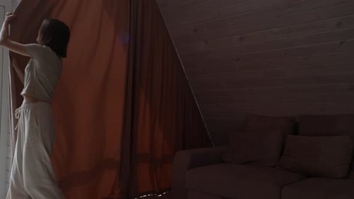 Stylish woman is closing big curtains in house