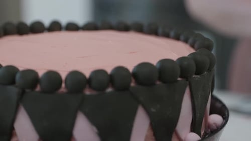 Close up, A pink and black decorated cake with a baker rolling fondant in the background.