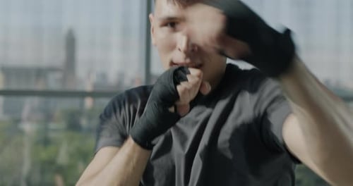 Slow Motion Portrait of Handsome Sportsman Training Boxing Moves in Gym Punching Air with Wrapped
