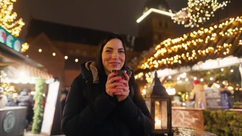 Une femme joyeuse dégustant une boisson chaude en se promenant dans un marché de Noël festif rempli de