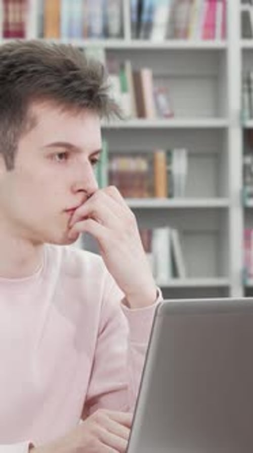 Thoughtful Young Man Engaged in Online Work at a Library