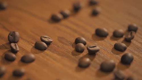 Frische Kaffeebohnen verstreut auf einem Holztisch in Zeitlupe.