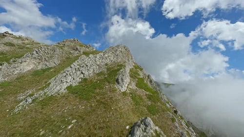 Rugged mountain peaks with rocky slopes and scattered greenery under blue skies , aerial view