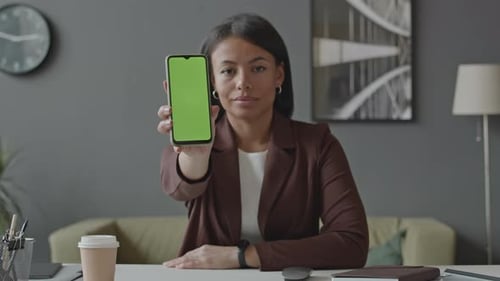 Woman Demonstrating Smartphone with Green Screen at Camera