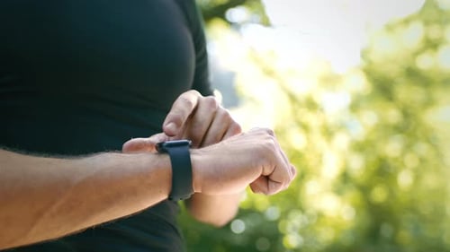 Young Man Checking Fitness Tracker While Jogging in Summer Park